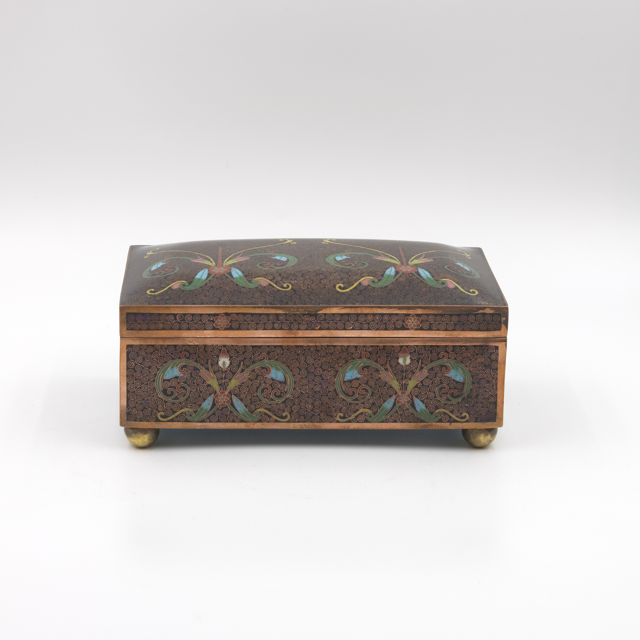 Cloisonné enamel box, three-quarter view, dark spiral ground with polychrome floral scrollwork, copper banding, ball feet