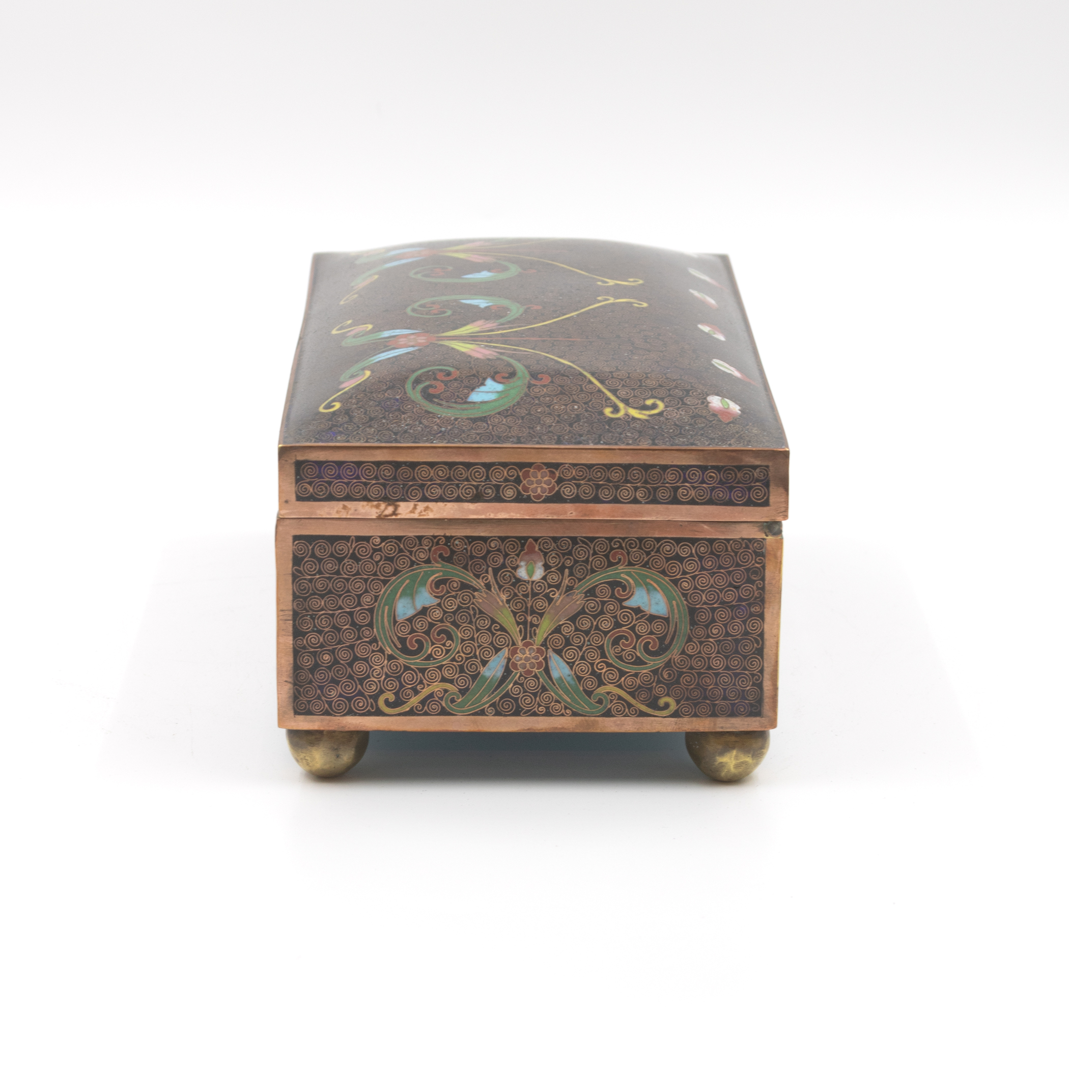 Cloisonné enamel box, end panel view showing centered foliate spray on dark spiral ground, copper banding, ball feet