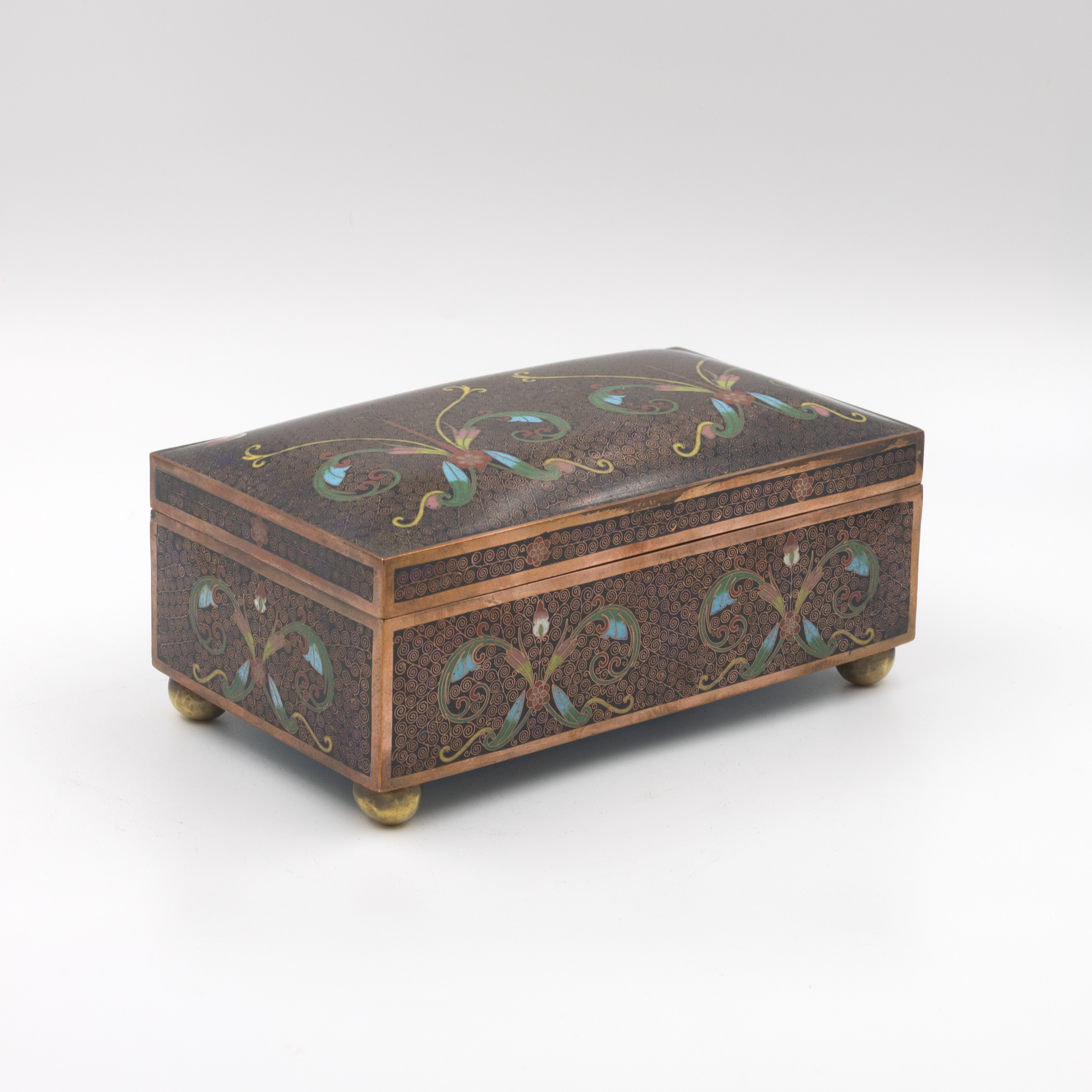 Cloisonné enamel box, three-quarter view, polychrome floral and foliate decoration on dark ground, copper banding and ball feet