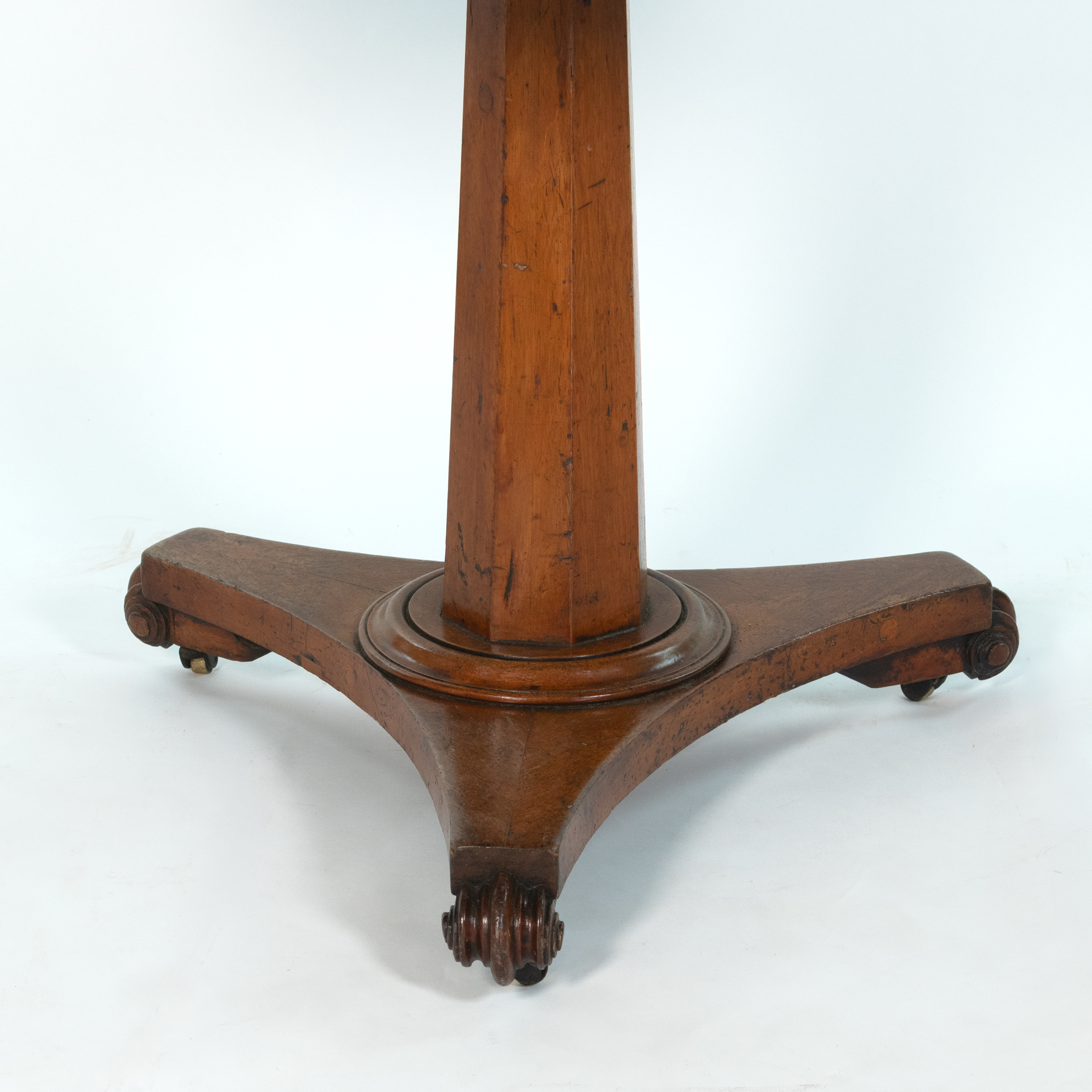 Close view of tripod base, scroll feet and castors on an English fruitwood center table, circa 1850