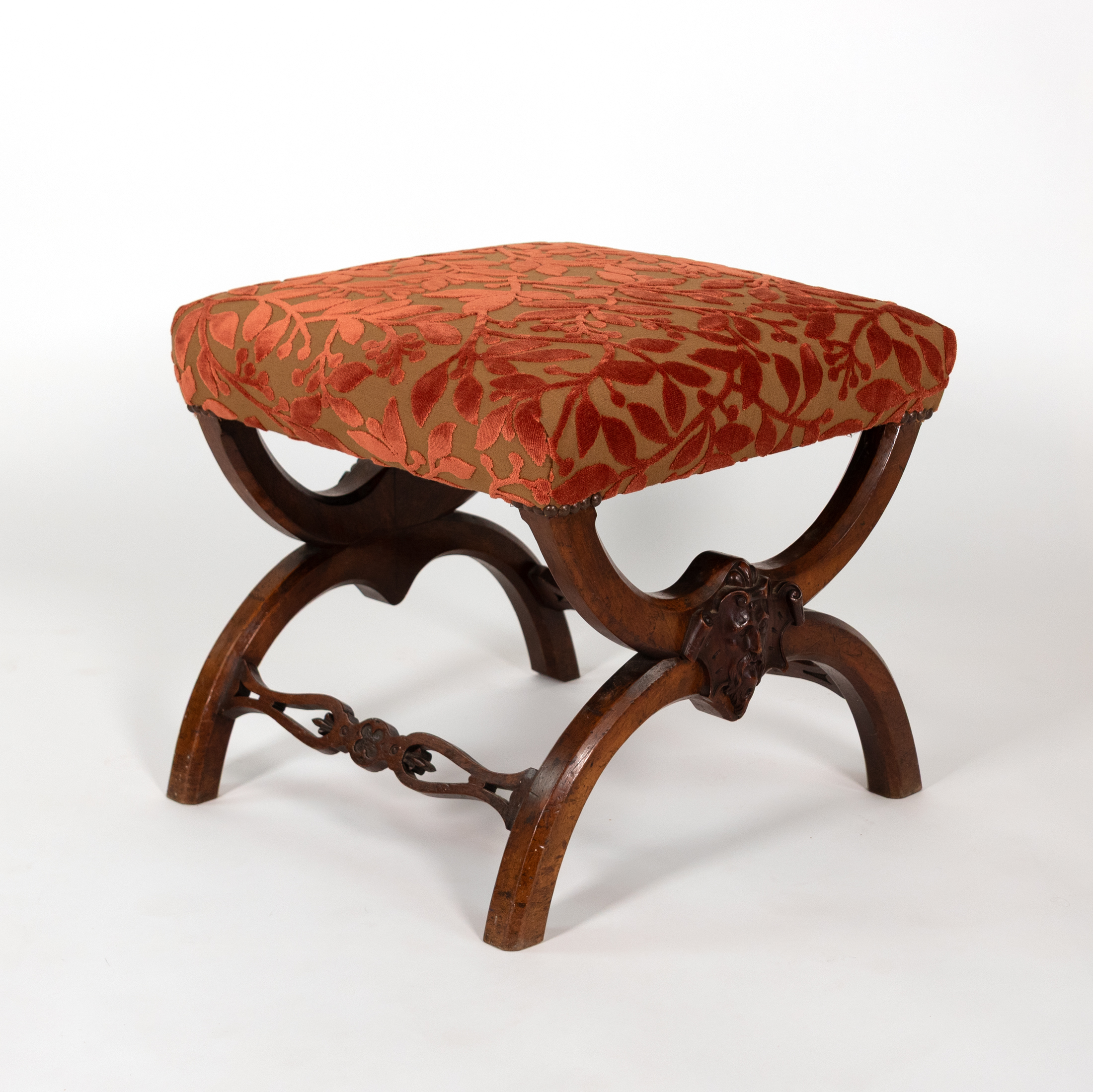 Carved walnut curule-form stool, three-quarter view with cut velvet seat and carved mask, French circa 1830