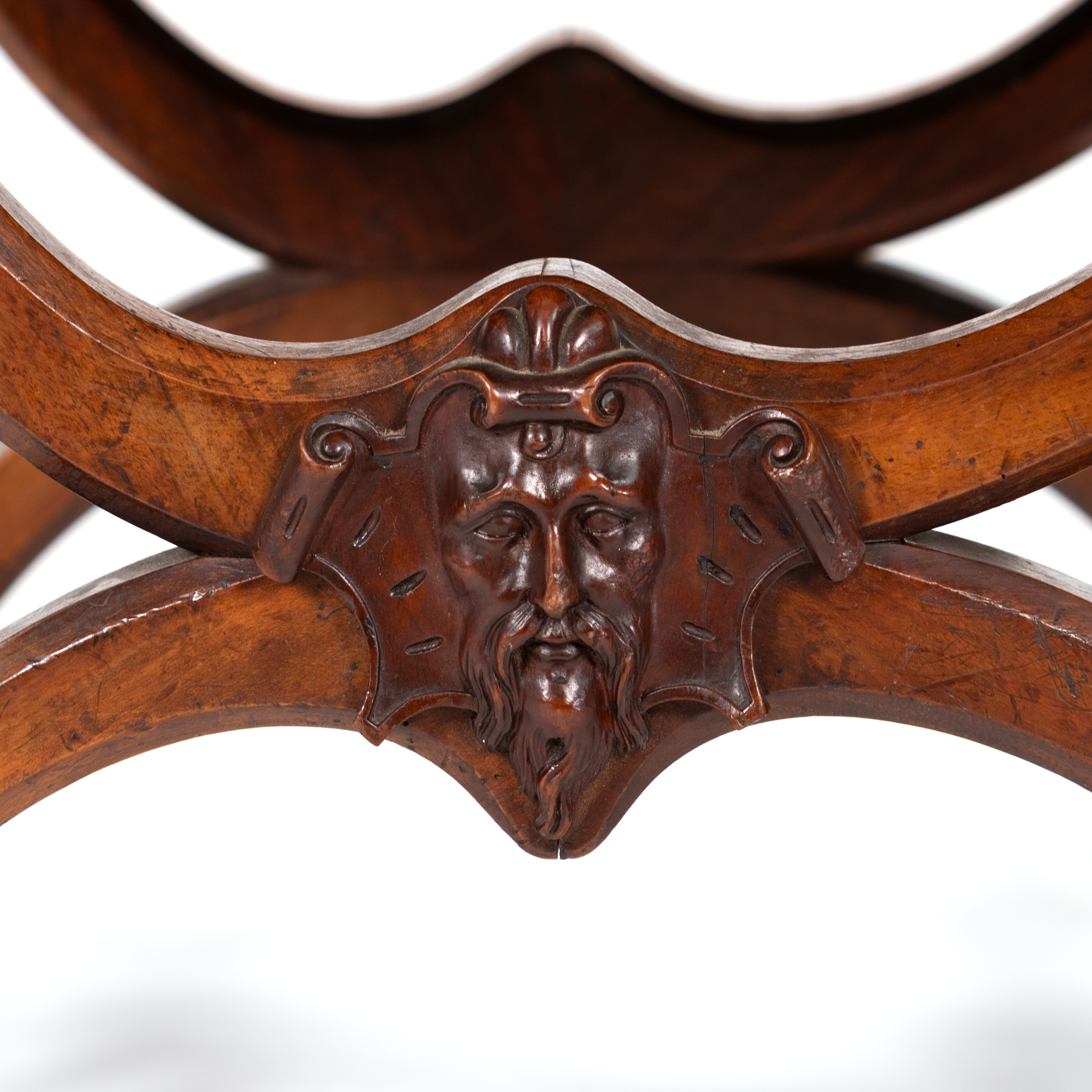Carved bearded mask on a French walnut curule-form stool, within a shield-shaped cartouche, circa 1830
