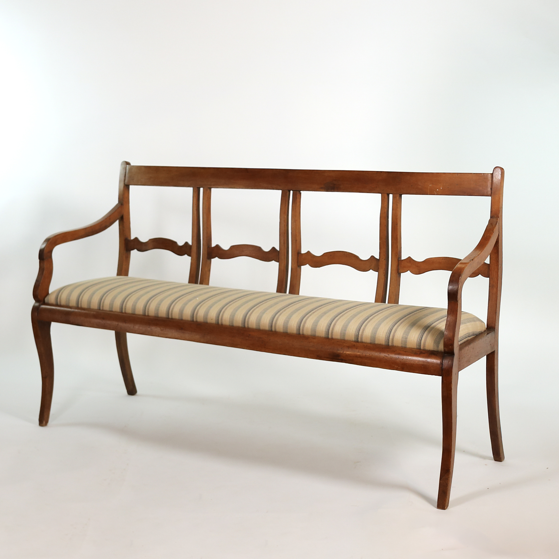 Three-quarter view of Italian walnut bench circa 1880 with curved open arms and sabre legs