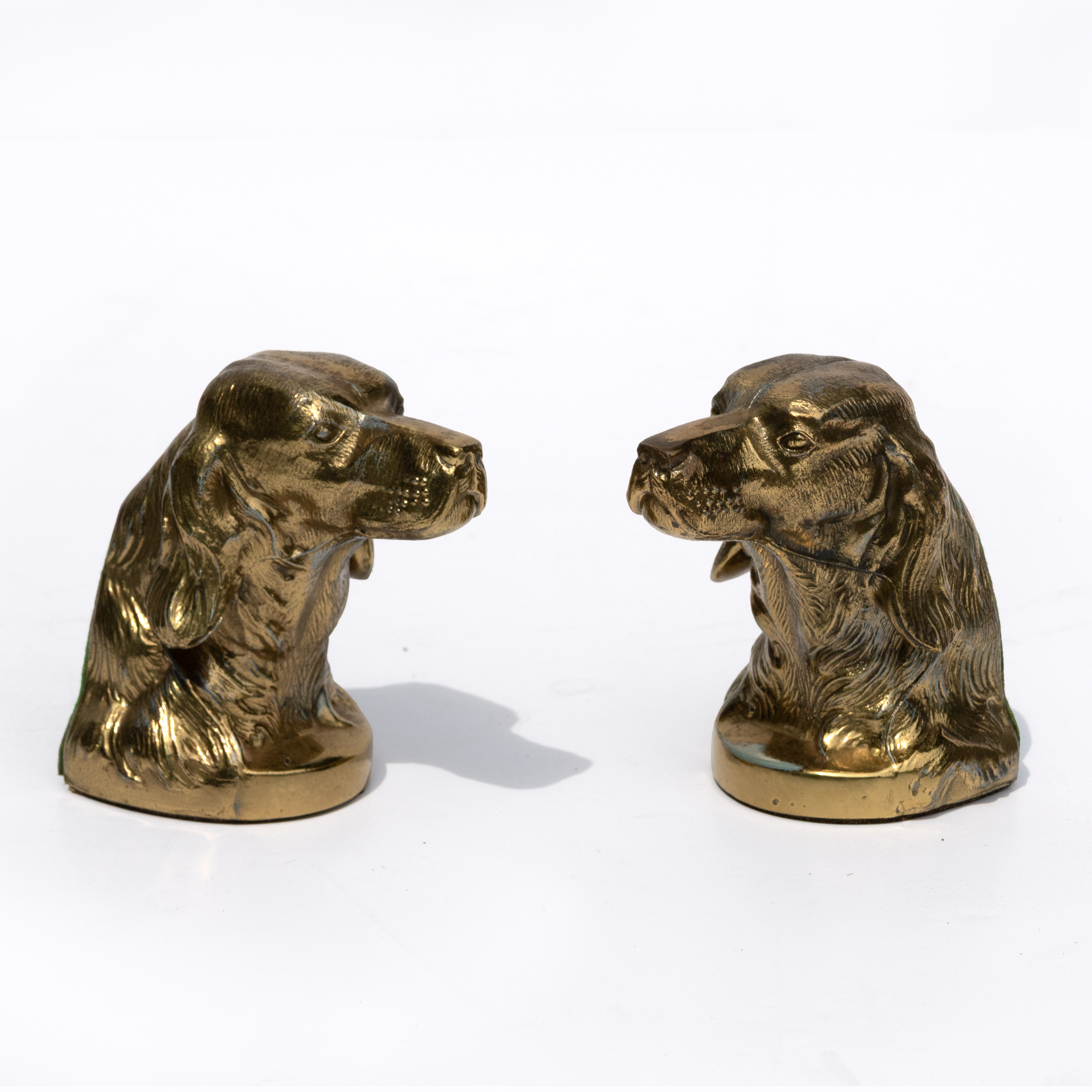 Pair of brass spaniel bookends modeled as opposing dog heads on a white background