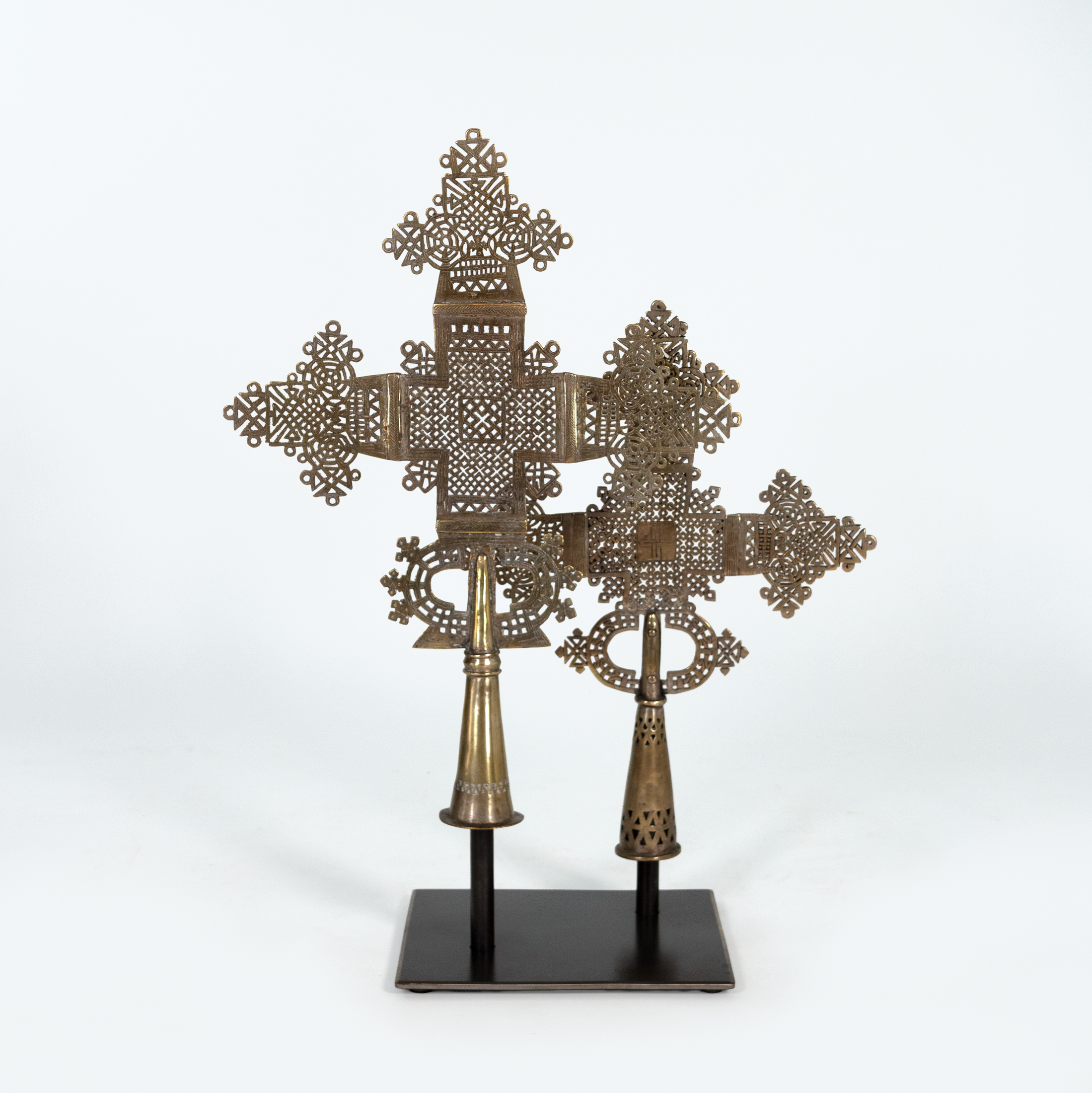 Two Ethiopian brass processional crosses with openwork latticework mounted on a steel stand