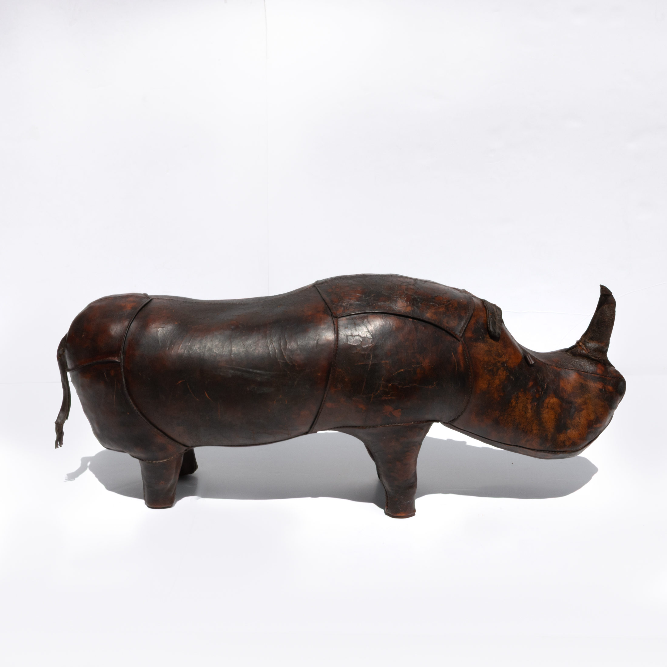 Dark brown leather rhinoceros footstool with stitched panels and four block feet, photographed with its surroundings visible.